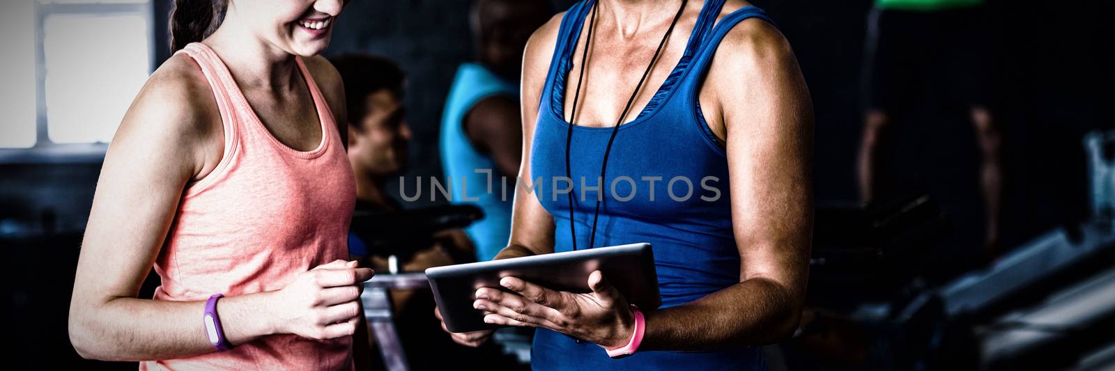 Smiling friends with digital tablet while standing in gym
