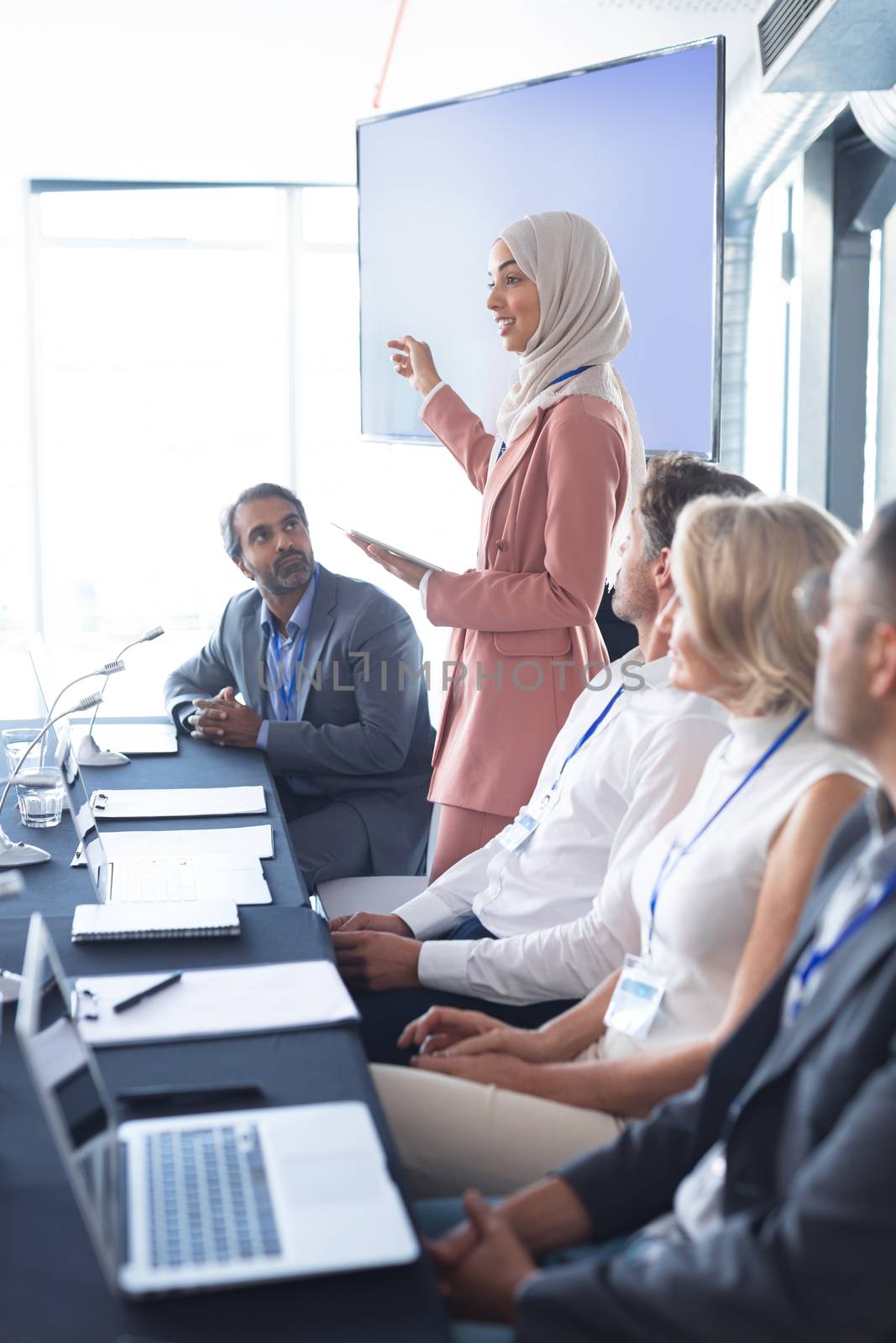 Side view of mixed race businesswoman in hijab giving presentation at table in business seminar. International diverse corporate business partnership concept