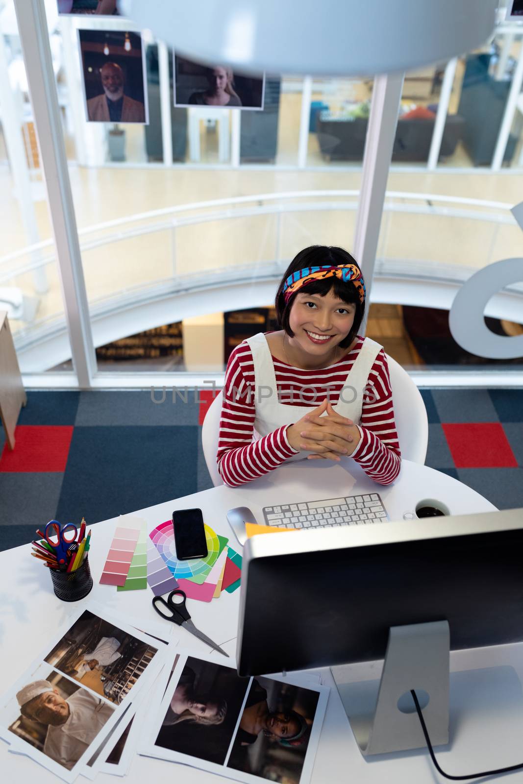 High angle view of pretty young Asian female graphic designer sitting at desk in office. This is a casual creative start-up business office for a diverse team