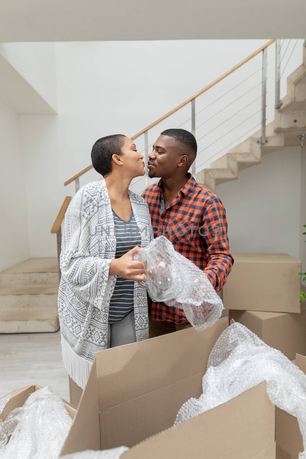 Front view of happy African american couple kissing each other while unpacking cardboard boxes in living room at home