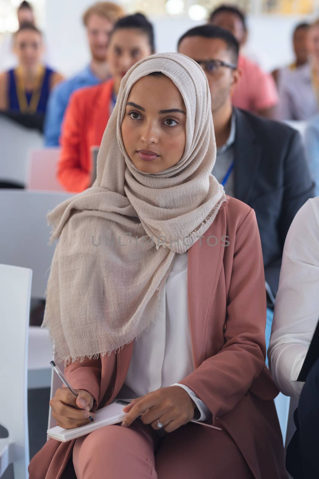 Close-up of mixed-race businesswoman in hijab listening to speaker in a business seminar. International diverse corporate business partnership concept