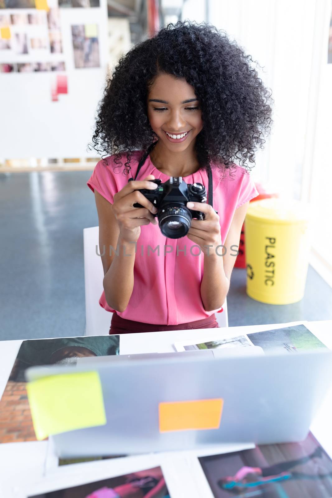 Front view of African american female graphic designer reviewing photos on digital camera at desk in office. This is a casual creative start-up business office for a diverse team