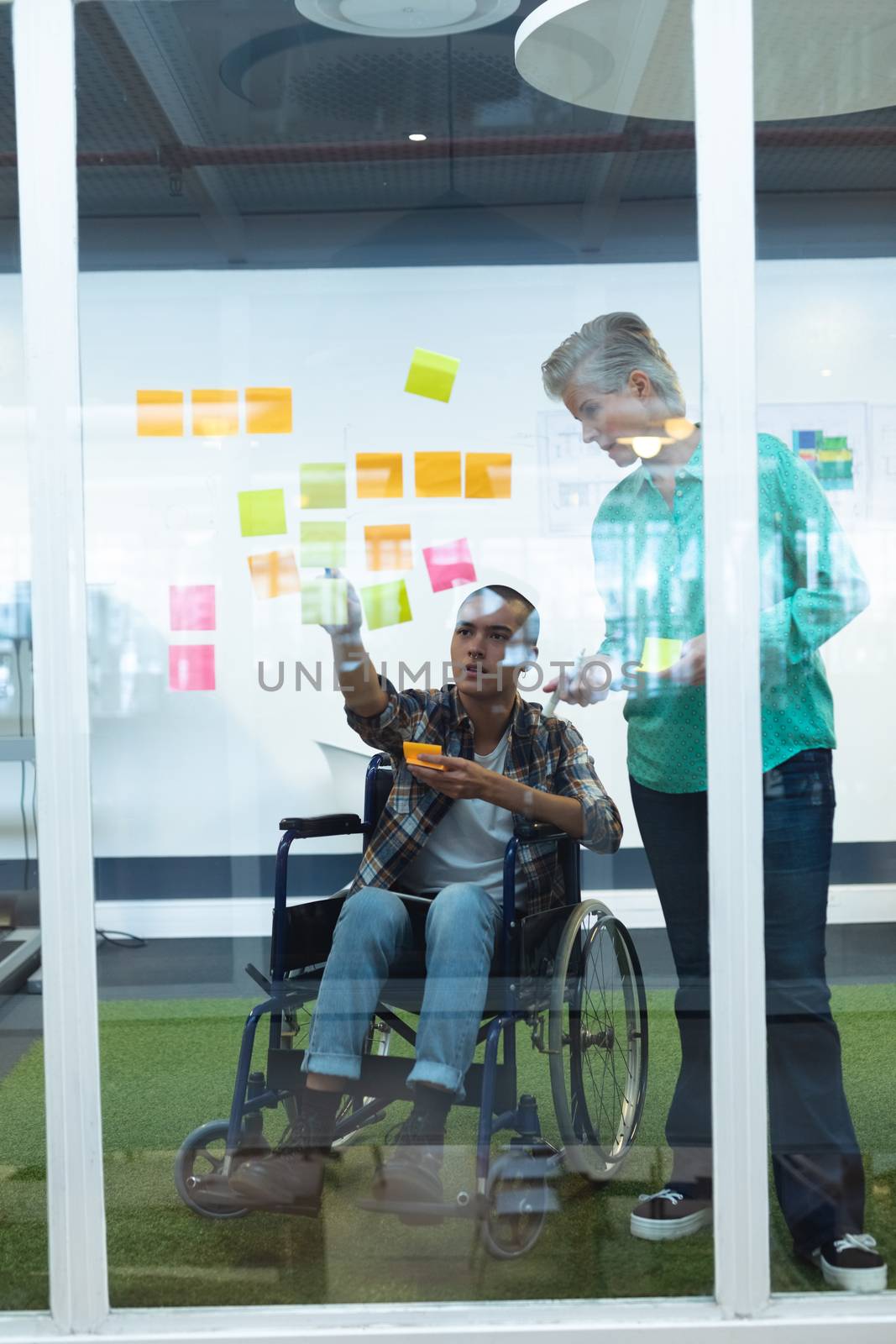 Front view of diverse executives discussing together over sticky notes in office. This is a casual creative start-up business office for a diverse team