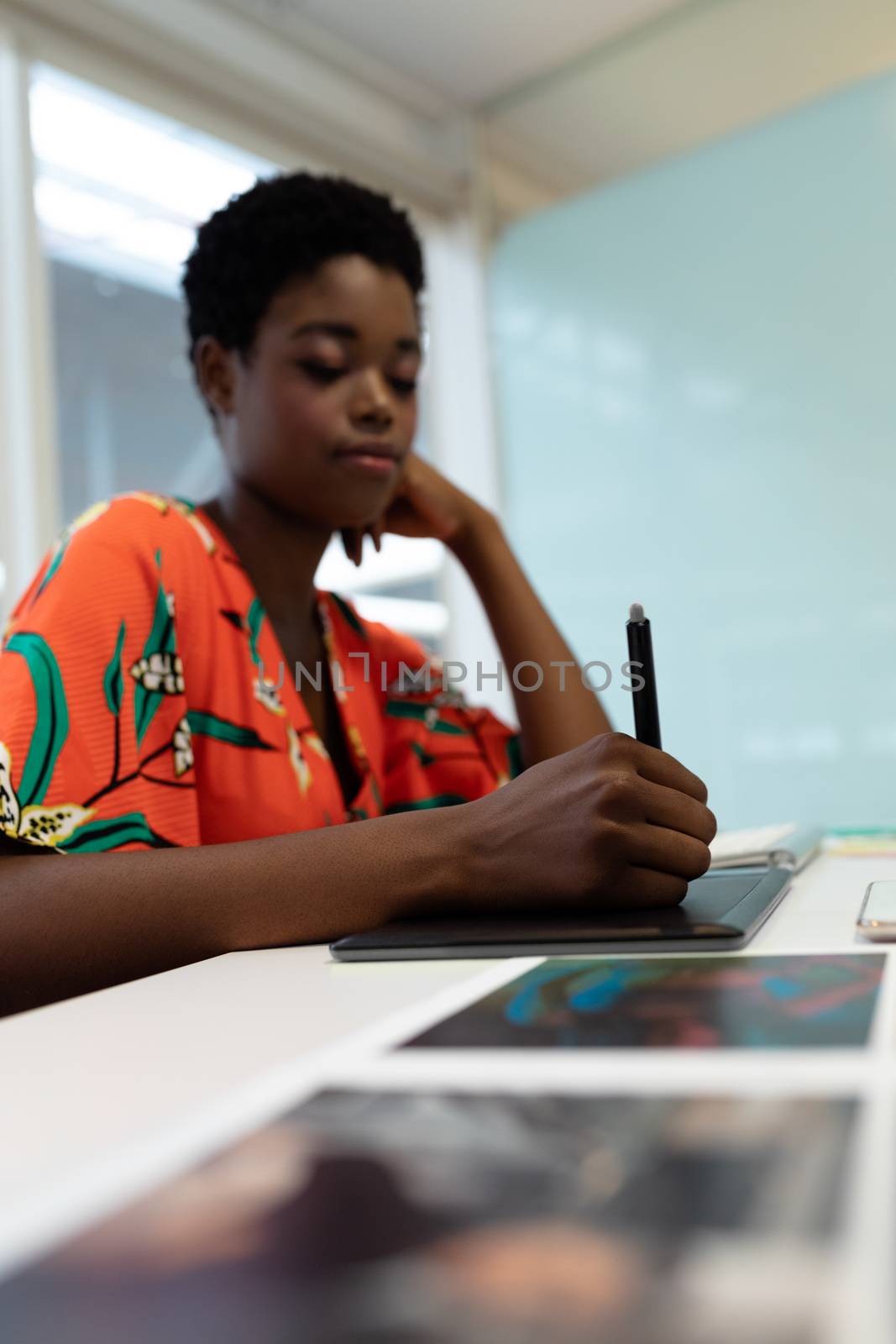 Side view of young pretty African american female graphic designer working on graphic tablet at desk in office. This is a casual creative start-up business office for a diverse team