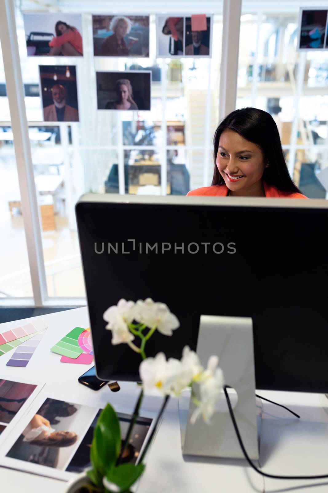 Front view of pretty young Asian female graphic designer working on computer at desk in office. This is a casual creative start-up business office for a diverse team