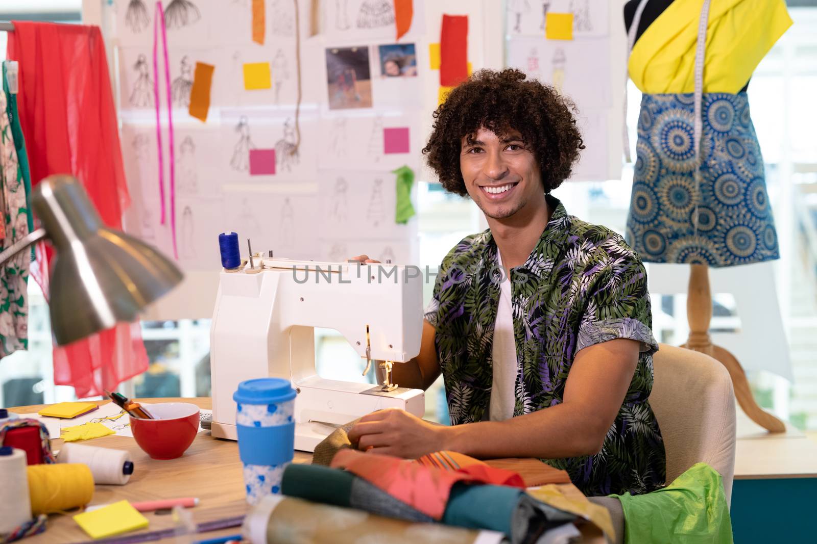 Portrait of young mixed race male fashion designer using sewing machine on a table in design studio. This is a casual creative start-up business office for a diverse team