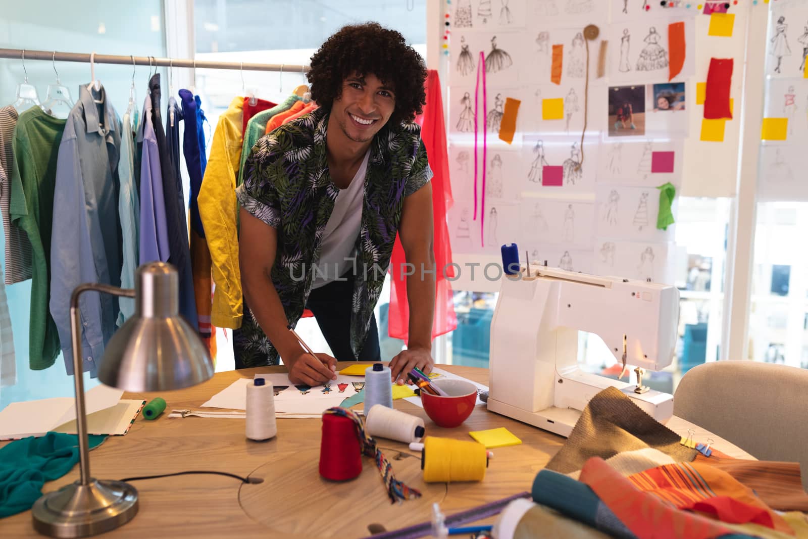 Front view of young handsome mixed race male fashion designer drawing a sketch at desk in design studio. This is a casual creative start-up business office for a diverse team