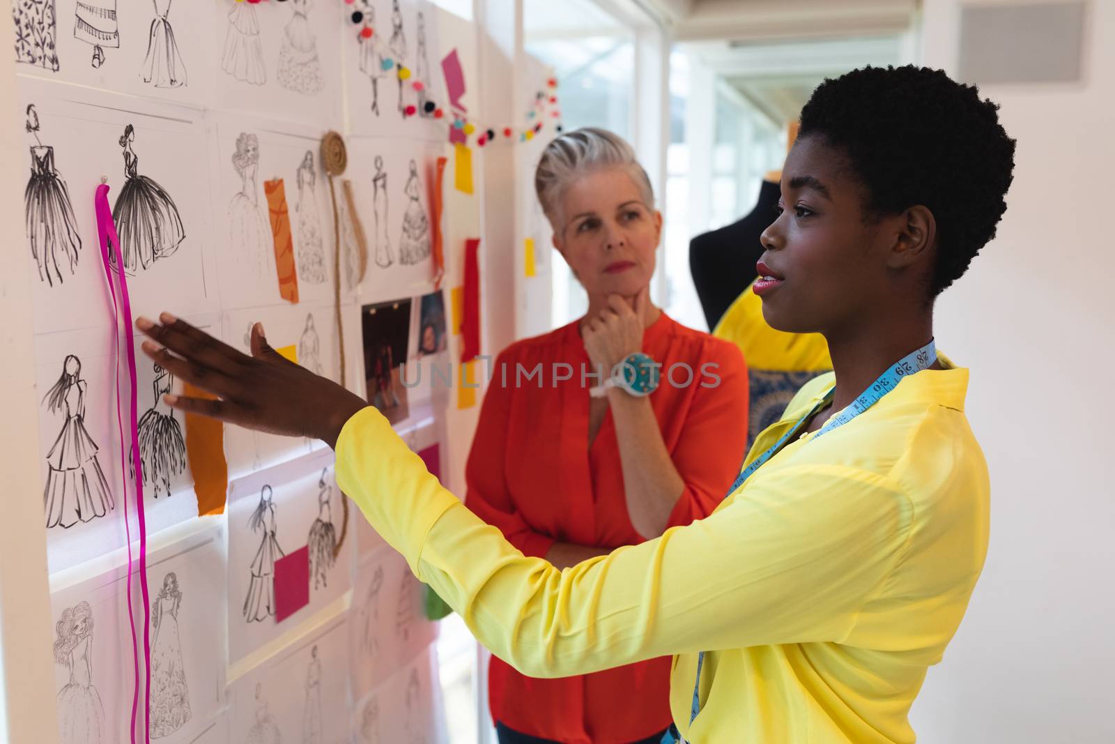 Side view of diverse female fashion designers discussing over sketch design in design studio. This is a casual creative start-up business office for a diverse team