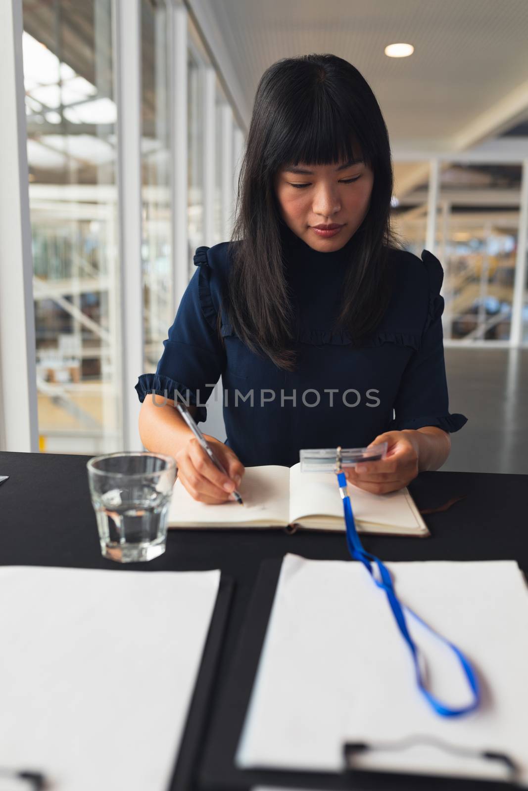 Front view of Asian Businesswoman noting id number on a diary at table in business seminar. International diverse corporate business partnership concept