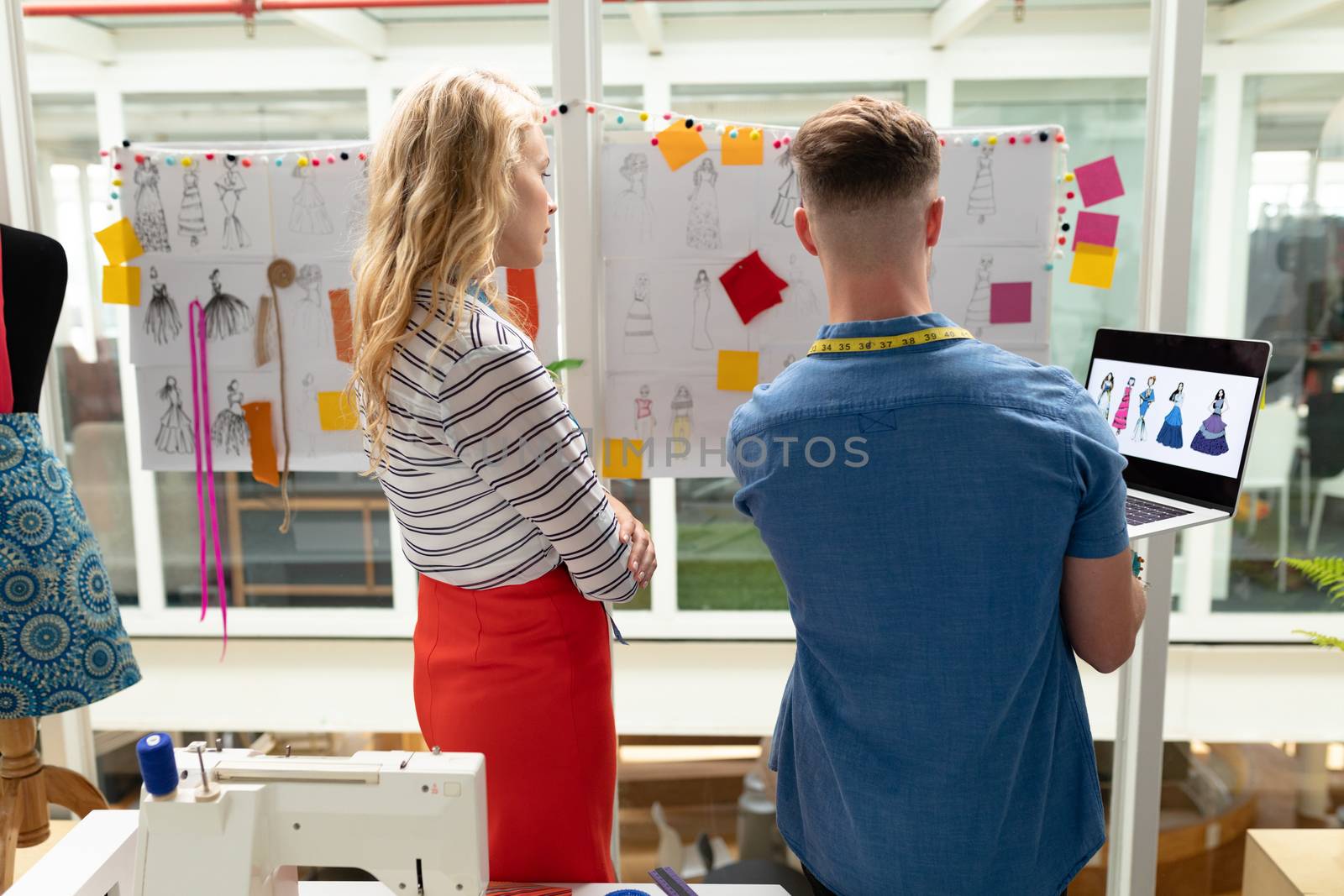 Rear view of Caucasian male and fashion designers discussing over sketch in design studio. This is a casual creative start-up business office for a diverse team