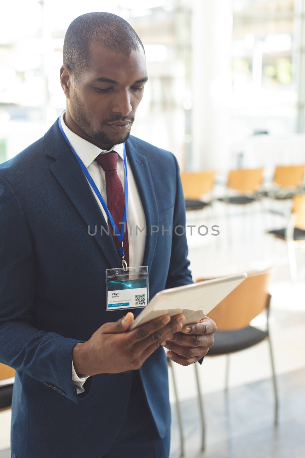 Side view of mature African-american businessman standing in empty conference room, watching digital tablet