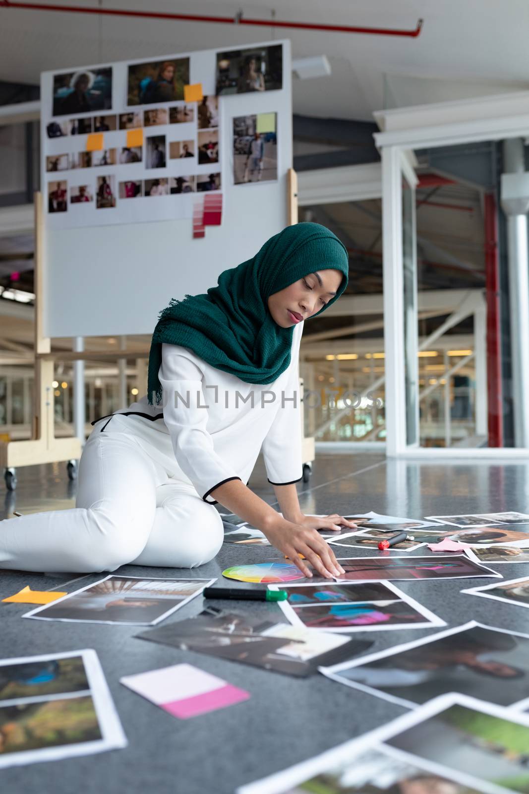 Female graphic designer in hijab checking photographs in office by Wavebreakmedia