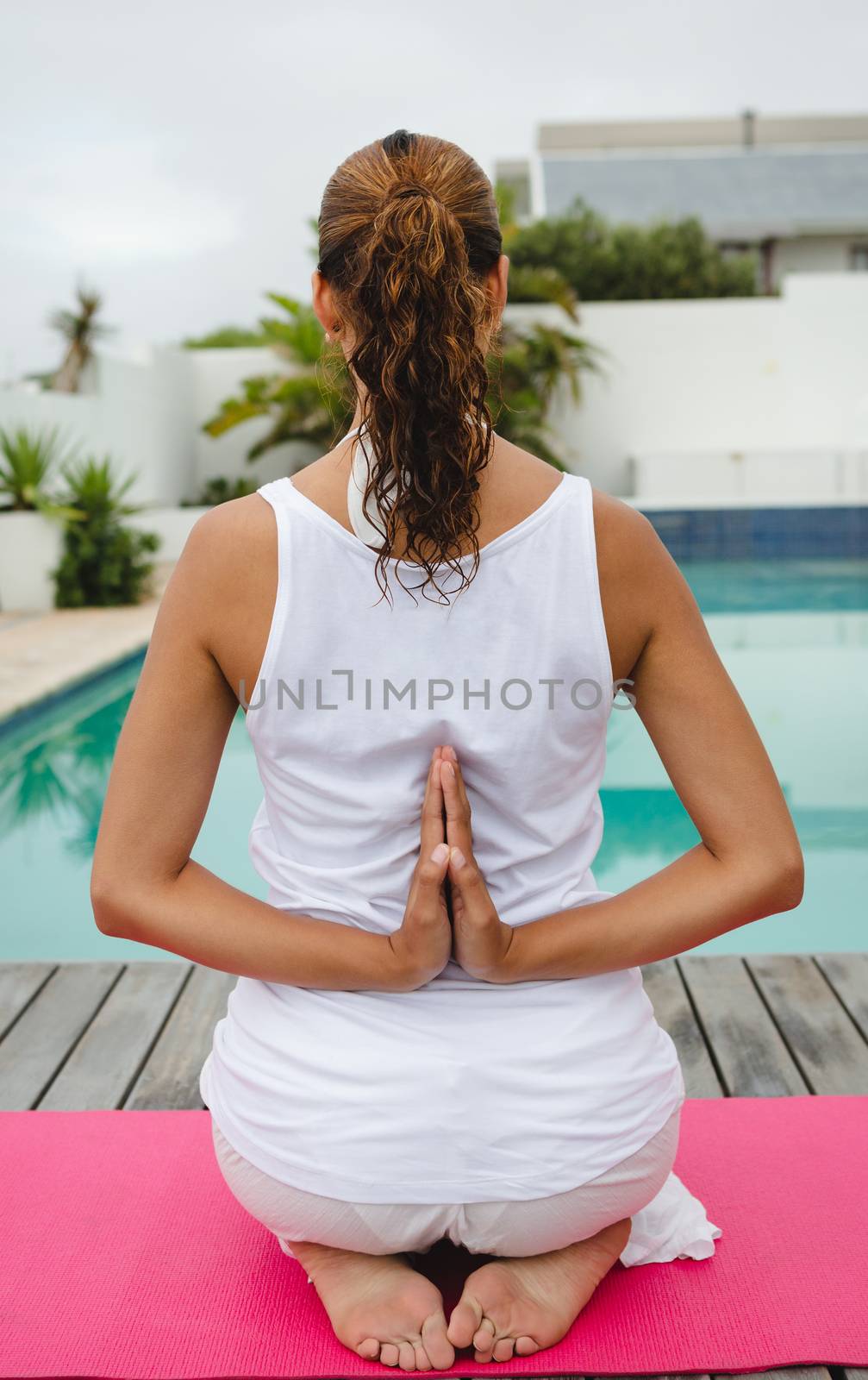 Rear view of mixed-race woman performing yoga near swimming pool in the backyard. Summer fun at home by the swimming pool