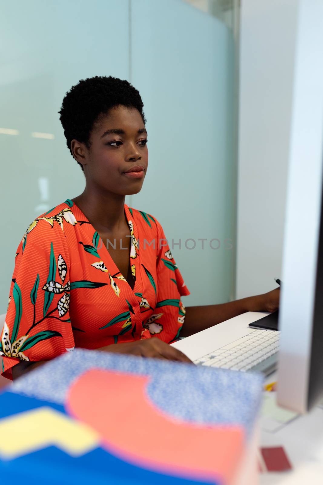 Side view of young pretty African american female graphic designer working on computer at desk in office. This is a casual creative start-up business office for a diverse team