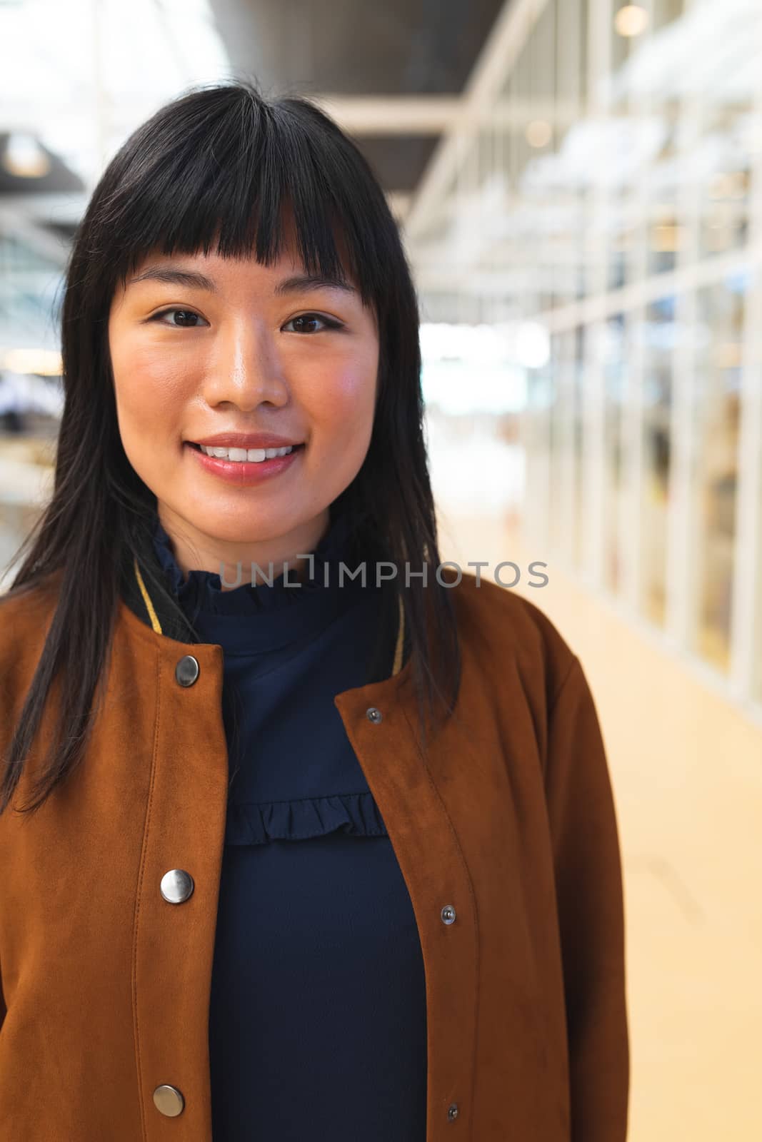 Close-up of happy Asian businesswoman looking at camera in the corridor at office. International diverse corporate business partnership concept