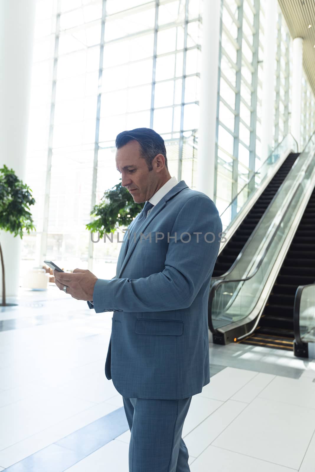 Side view of mature Caucasian businessman looking at mobile phone while standing in modern office