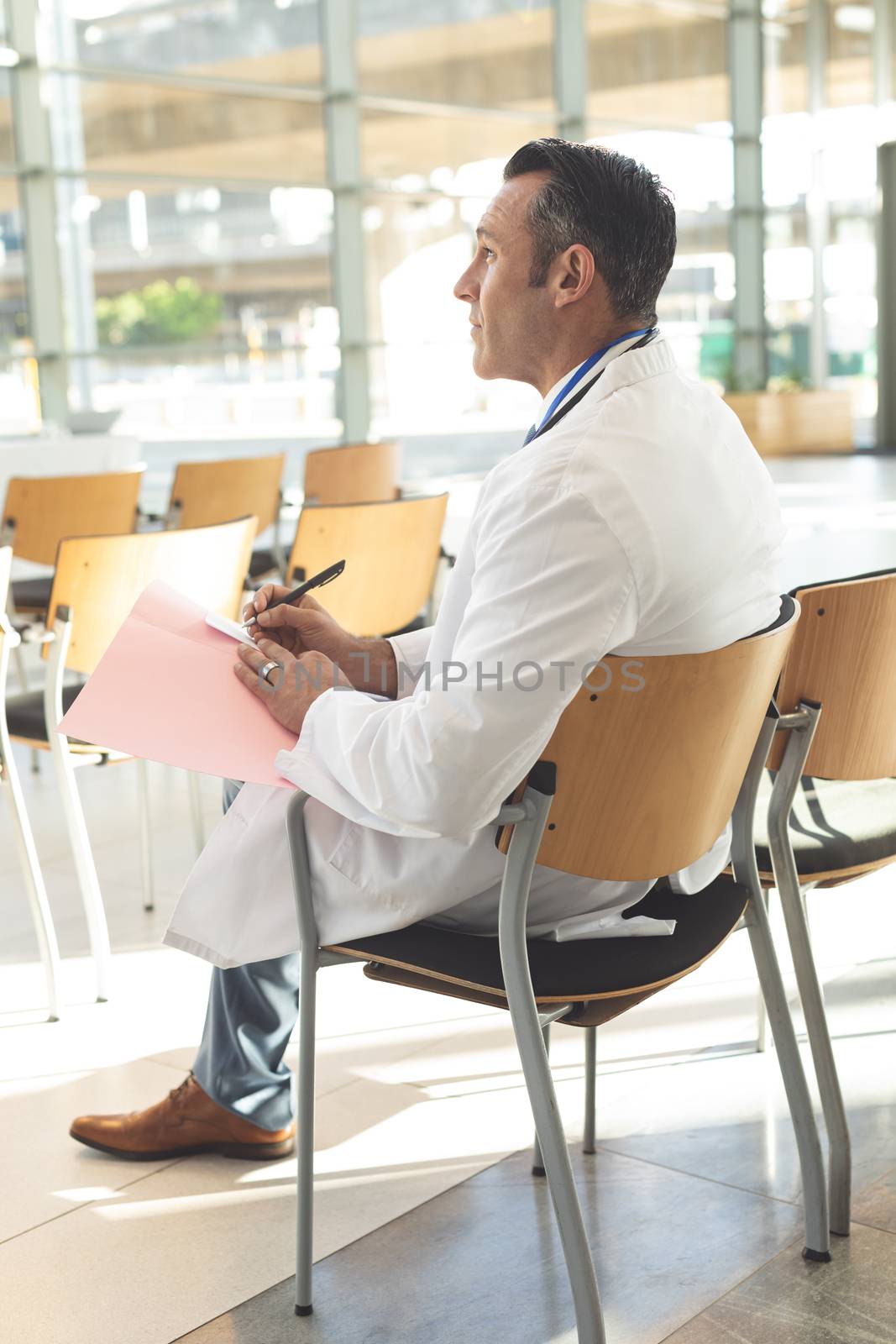 Side view of mature male executive sat in empty conference room thinking while writing on folder