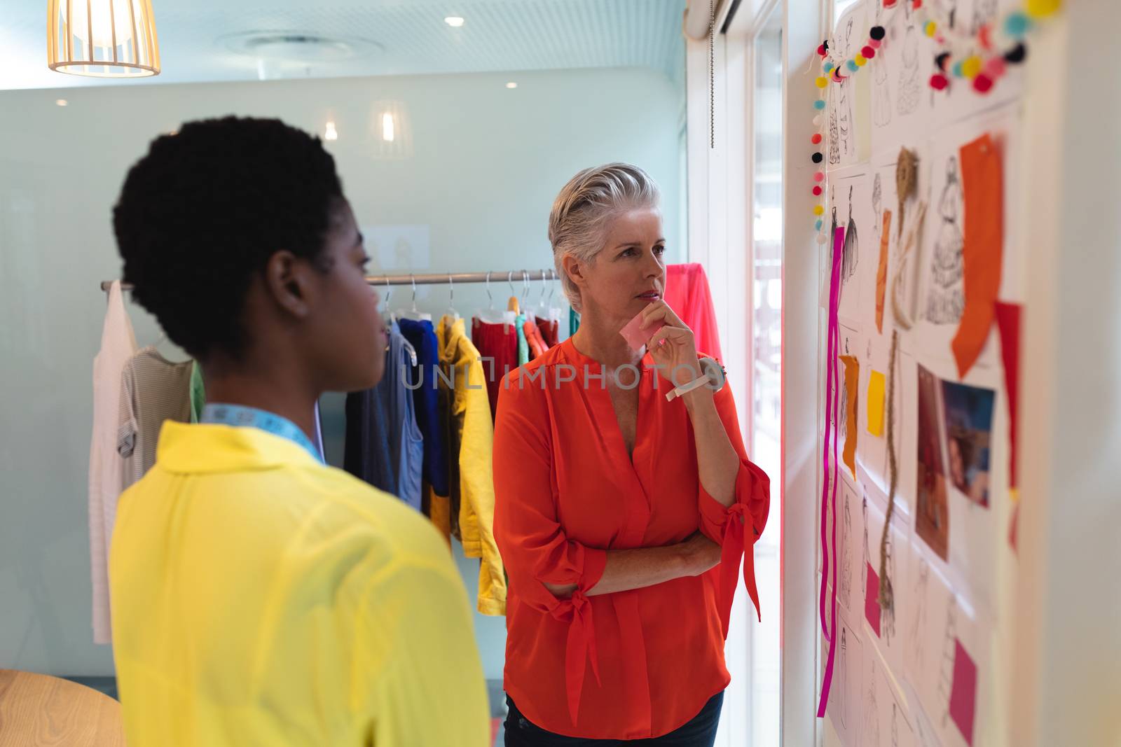 Side view of thoughtful diverse female fashion designers looking over sketch design in design studio. This is a casual creative start-up business office for a diverse team