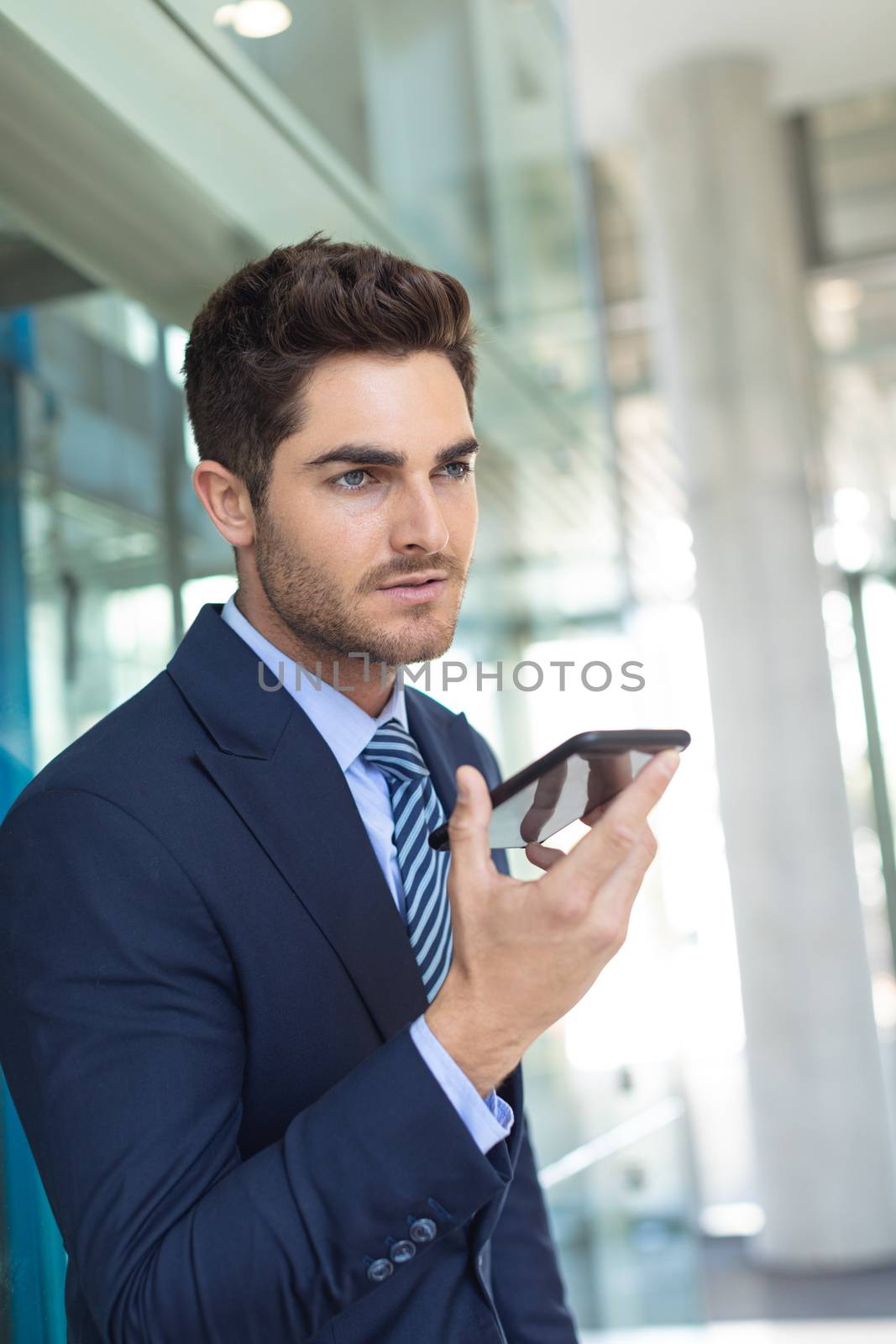 Side view of young Caucasian businessman speaking on mobile phone while standing in modern office