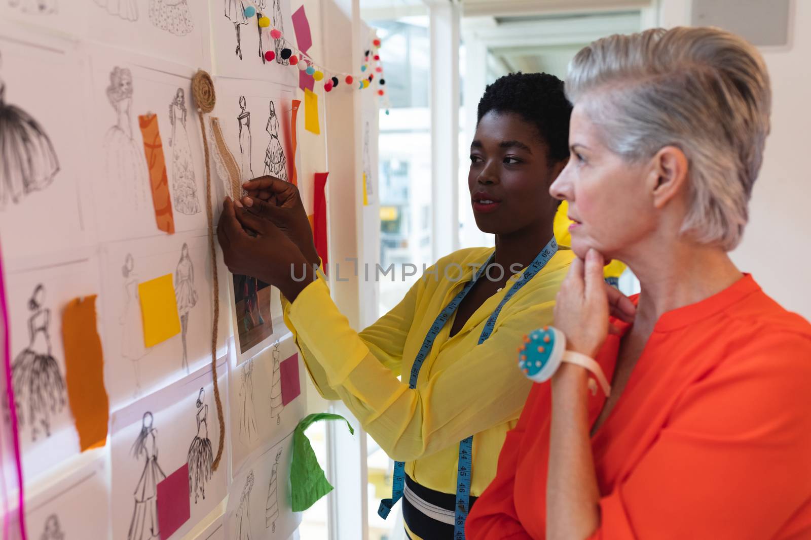 Side view of diverse female fashion designers discussing over sketch design in design studio. This is a casual creative start-up business office for a diverse team