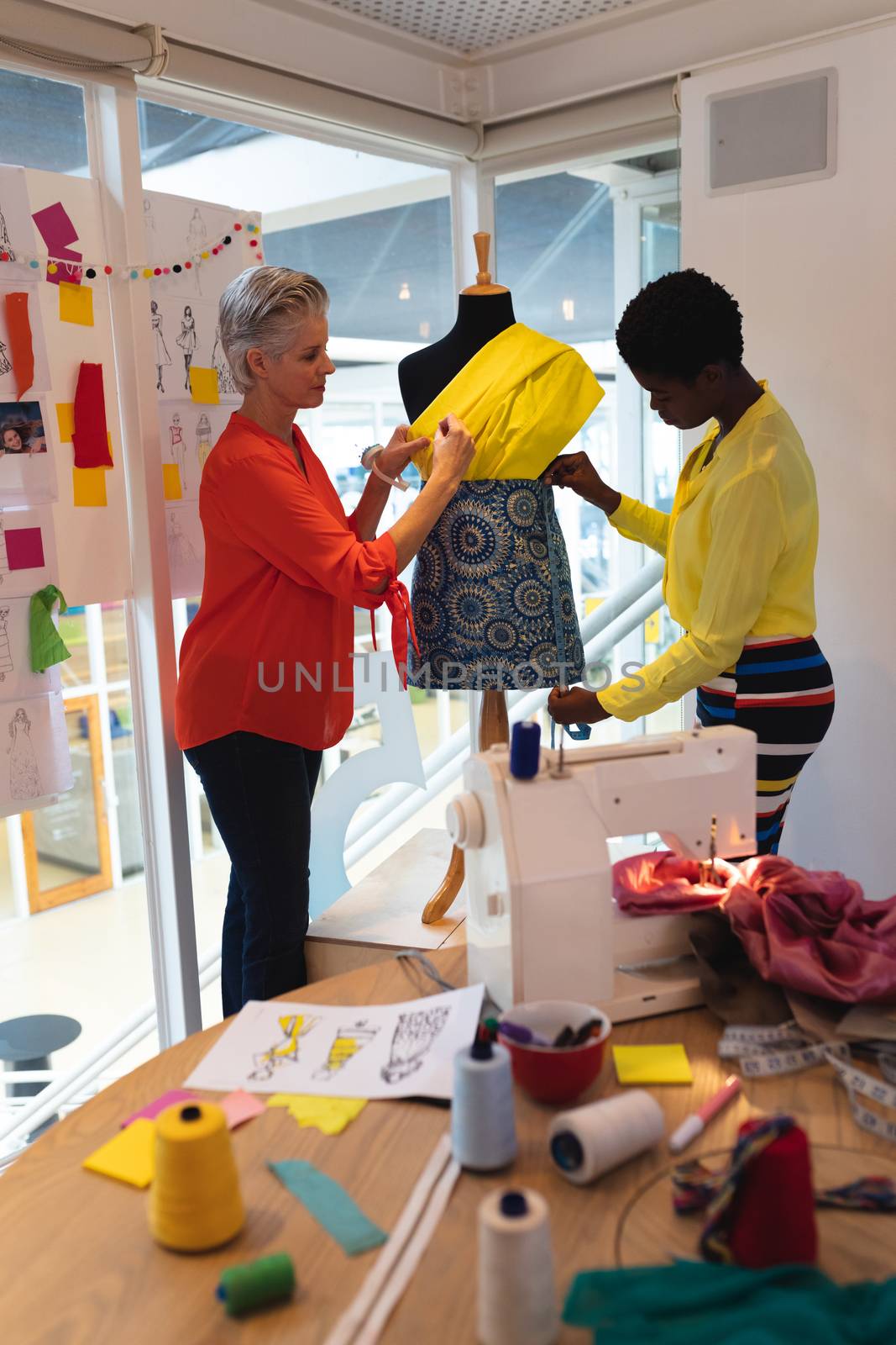 Side view of diverse female graphic designers using measuring tape on a mannequin in design studio. This is a casual creative start-up business office for a diverse team