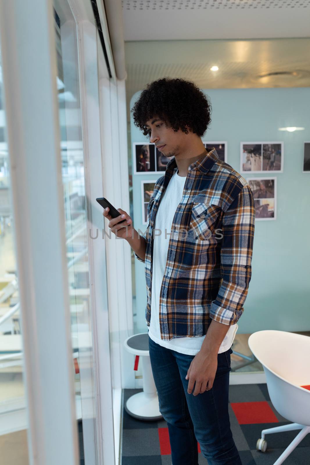 Side view of young mixed-race male graphic designer using mobile phone in office. This is a casual creative start-up business office for a diverse team