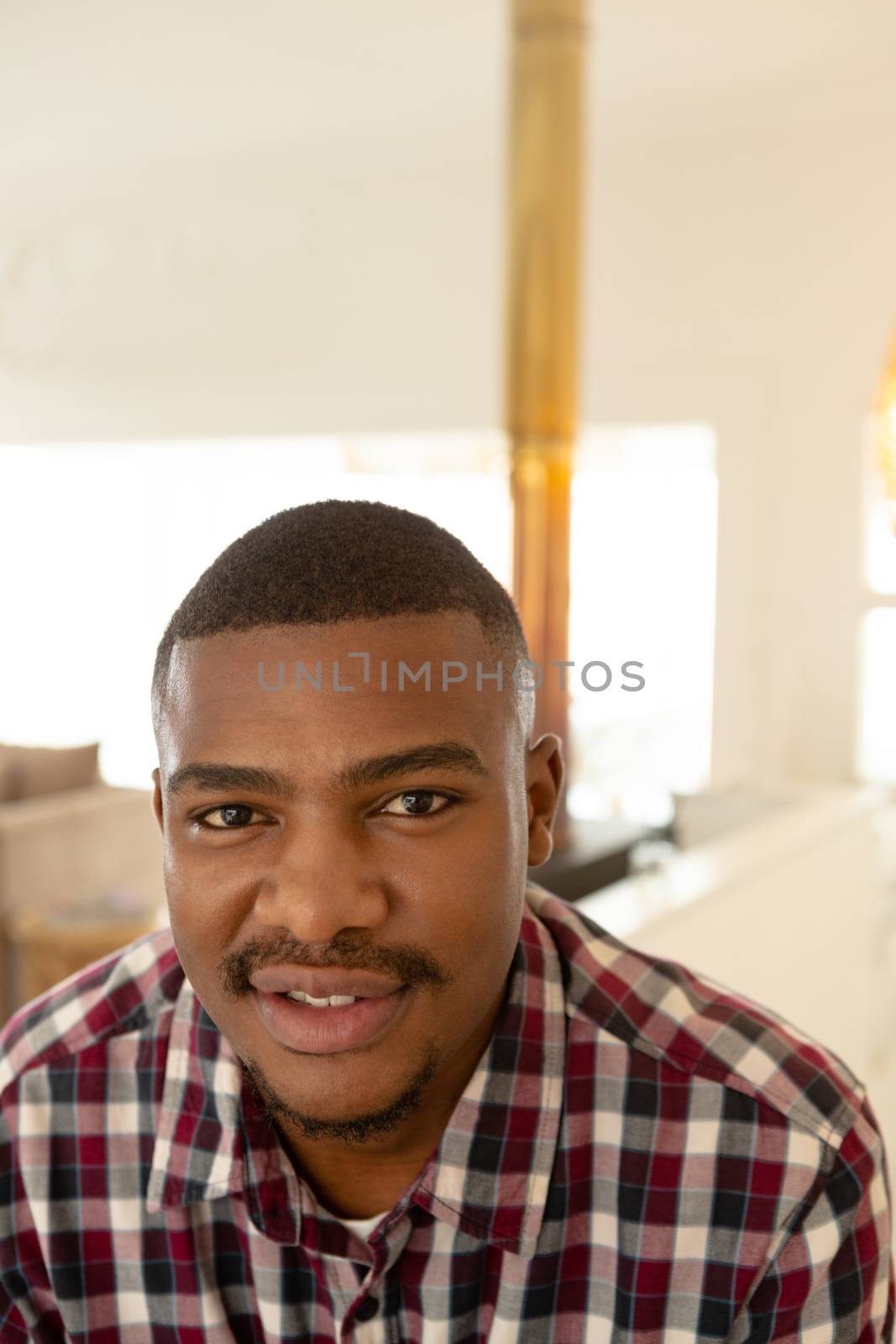 Close-up of happy African-american man looking at camera in a comfortable home. Authentic home lifestyle setting with young African American male