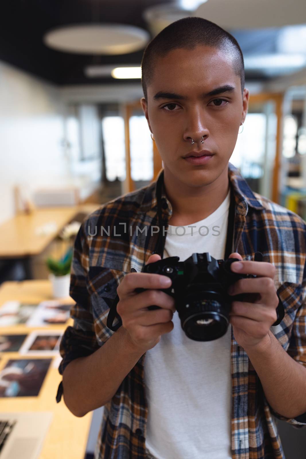 Portrait of mixed race male graphic designer holding a camera in office. This is a casual creative start-up business office for a diverse team