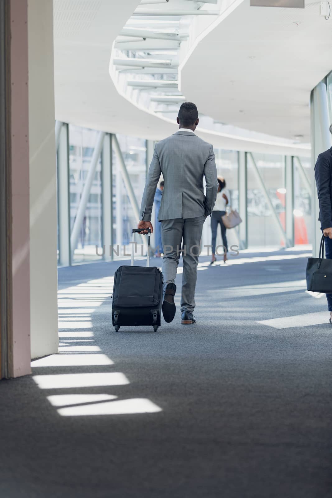 Rear view of African american businessman walking in corridor with suitcase in modern office