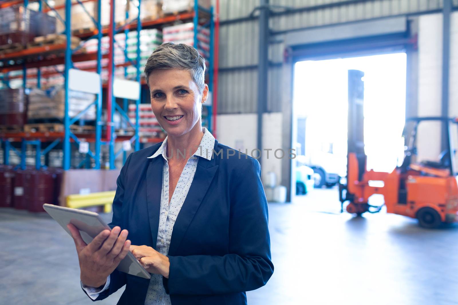 Manager looking at camera while using digital tablet in warehouse by Wavebreakmedia