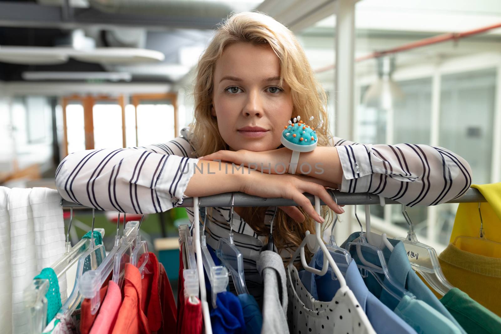 Portrait of Caucasian female fashion designer leaning on clothes rack in design studio. This is a casual creative start-up business office for a diverse team
