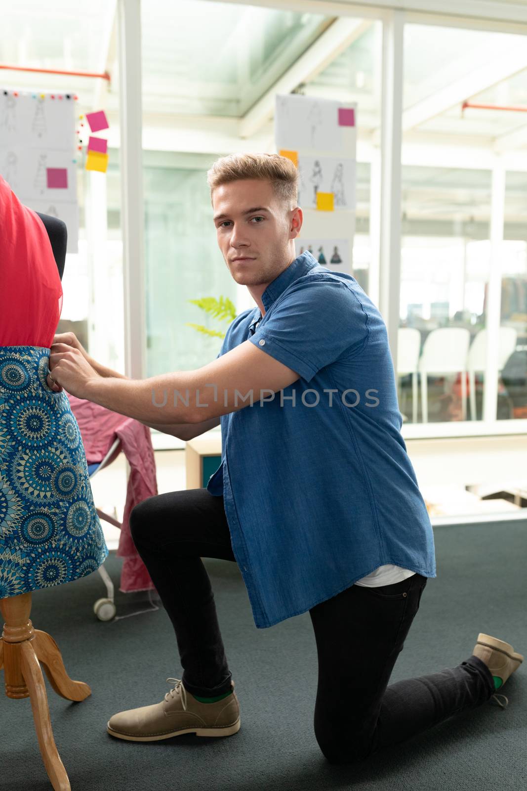 Portrait of Caucasian male fashion designer dressing a mannequin in design studio. This is a casual creative start-up business office for a diverse team