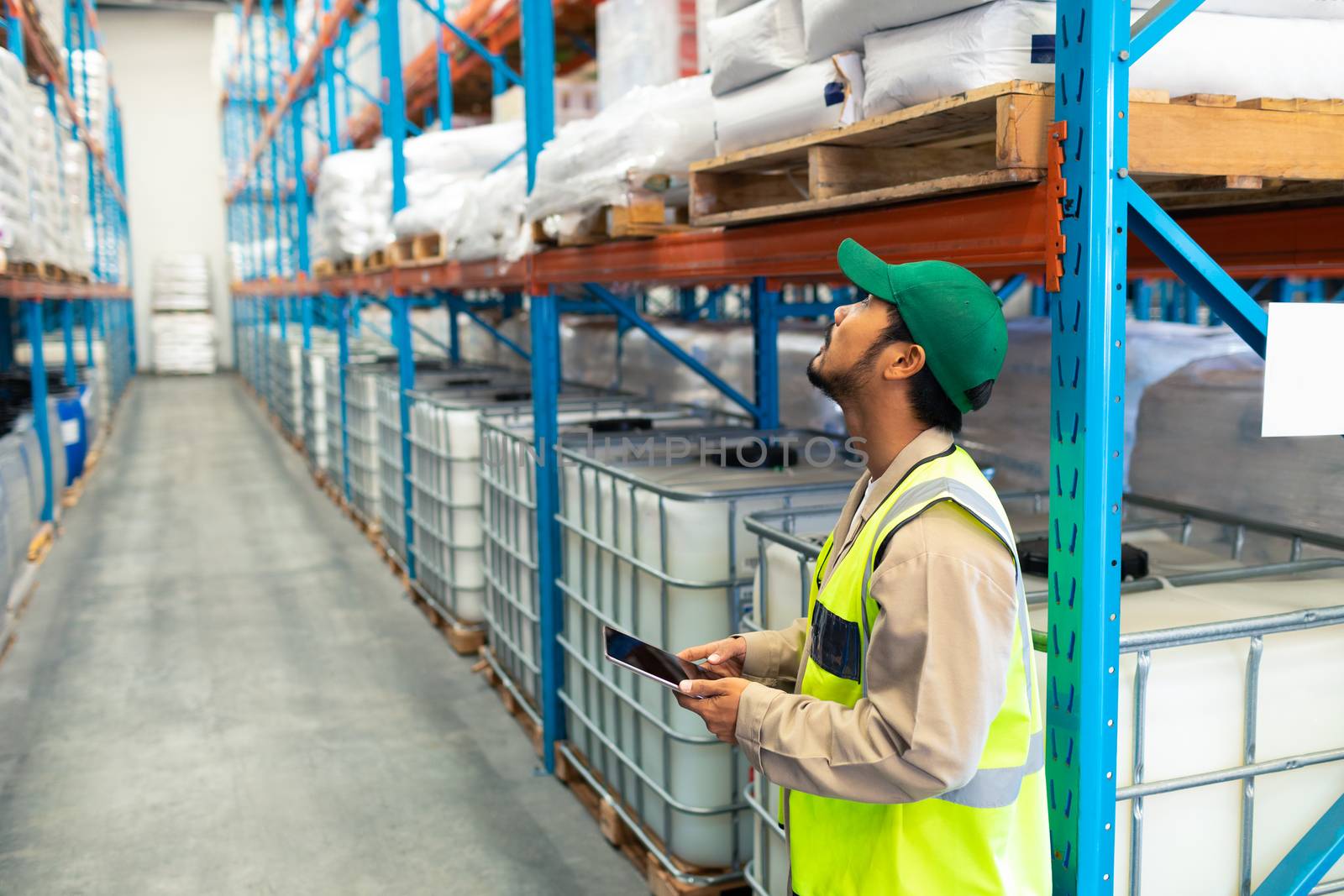 Side view of handsome mature Asian male worker with digital tablet working in warehouse. This is a freight transportation and distribution warehouse. Industrial and industrial workers concept