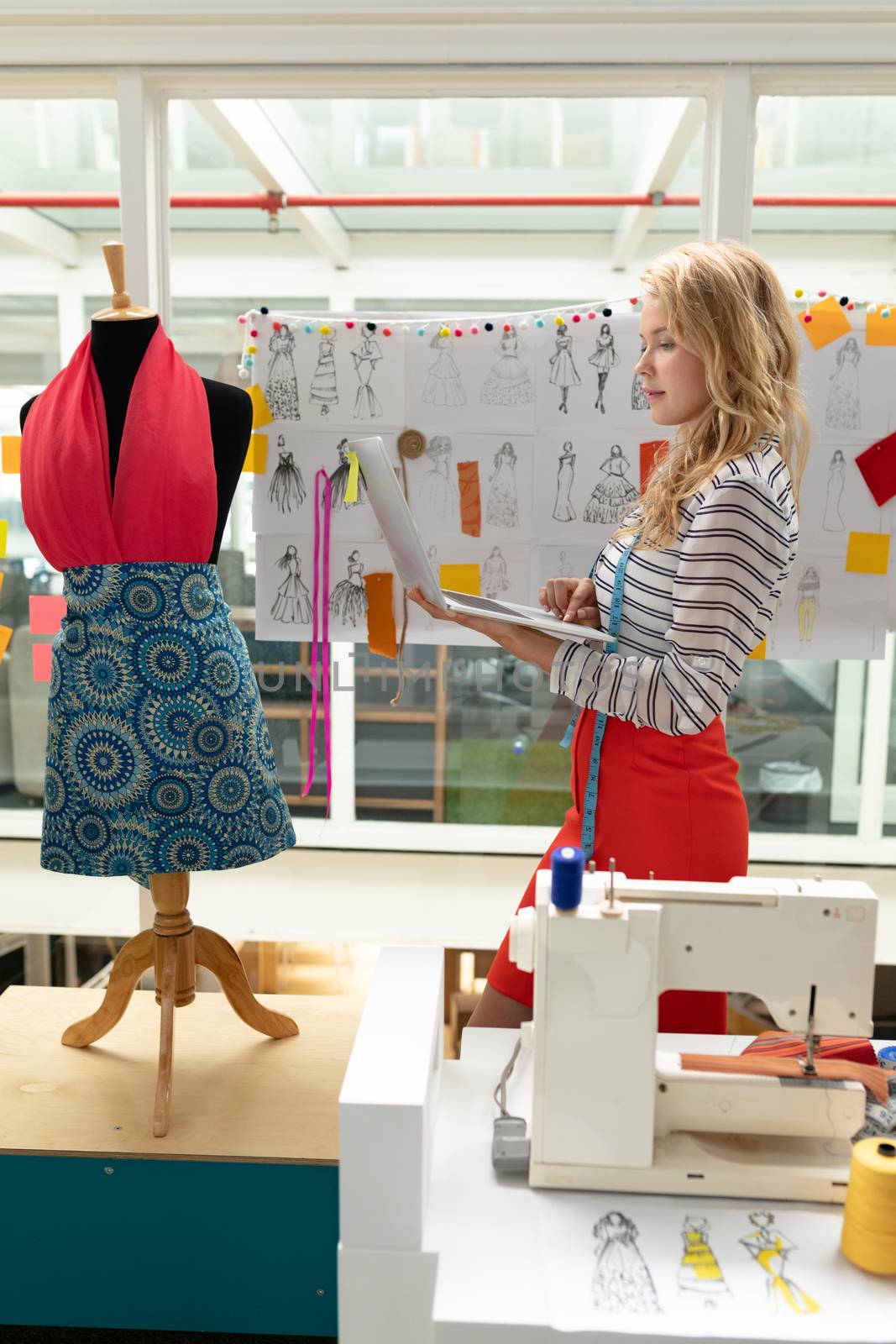 Side view of beautiful Caucasian female fashion designer using laptop in design studio. This is a casual creative start-up business office for a diverse team