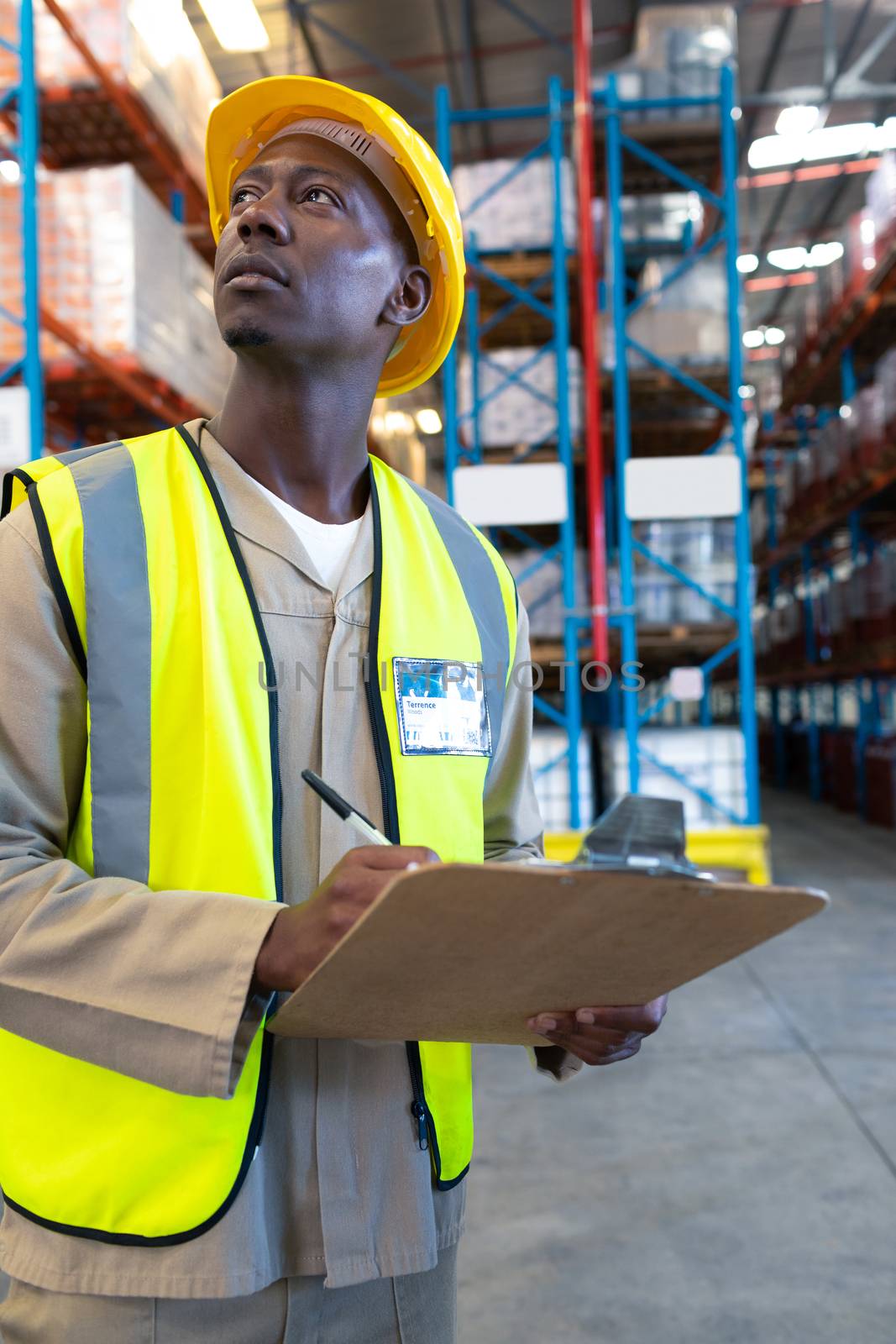 Close-up of concentrated African-american male worker looking away while writing on clipboard in warehouse. This is a freight transportation and distribution warehouse. Industrial and industrial workers concept