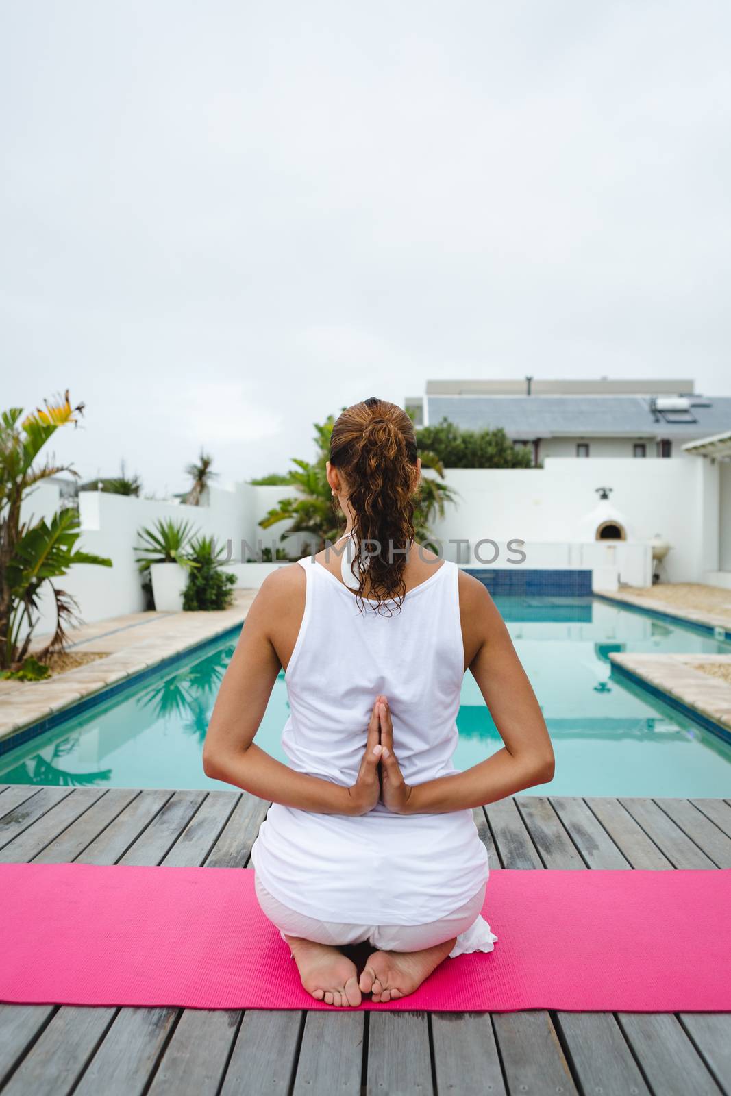 Rear view of beautiful mixed-race woman performing yoga near swimming pool in the backyard. Summer fun at home by the swimming pool