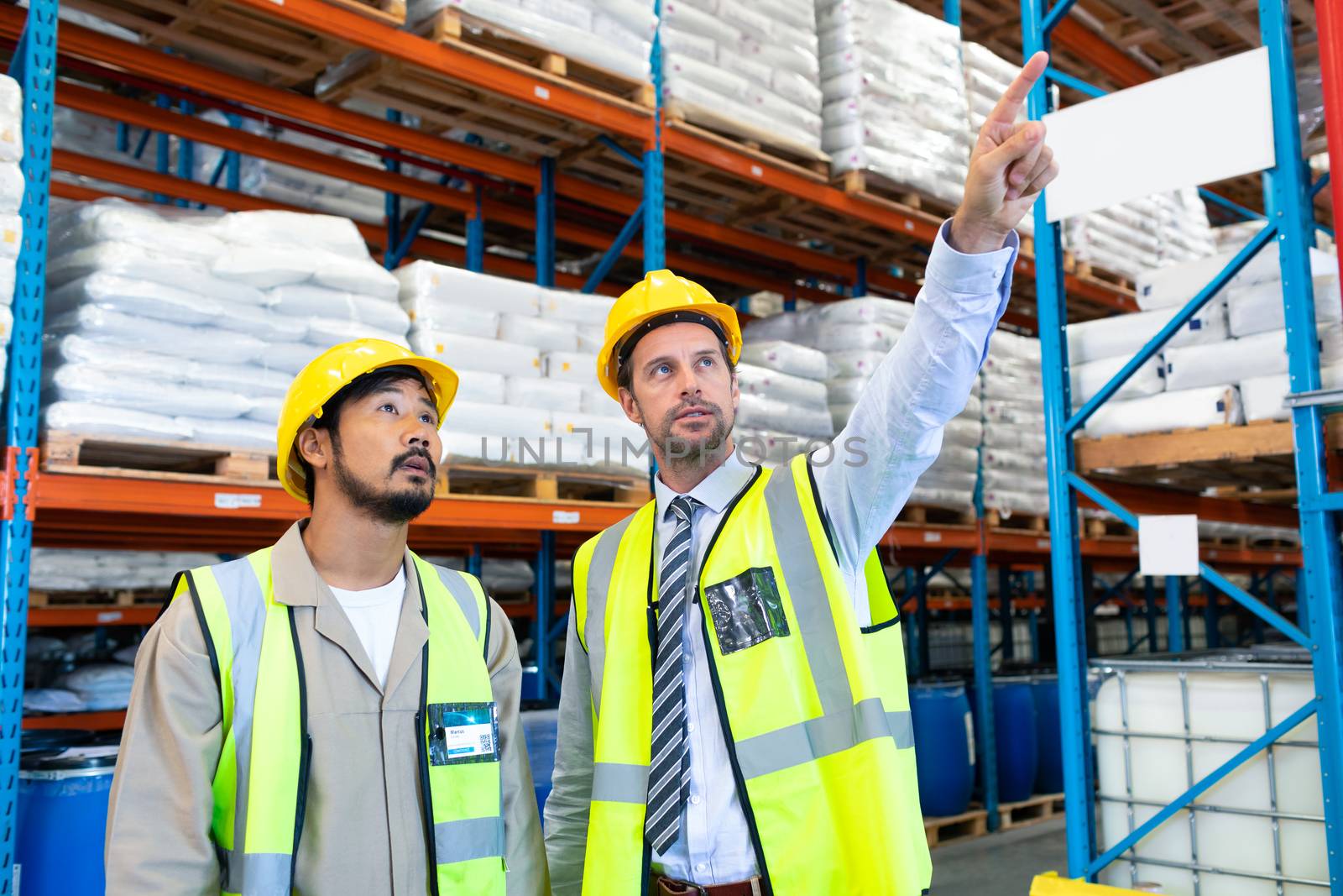 Male supervisor standing with worker and pointing at distance in warehouse  by Wavebreakmedia