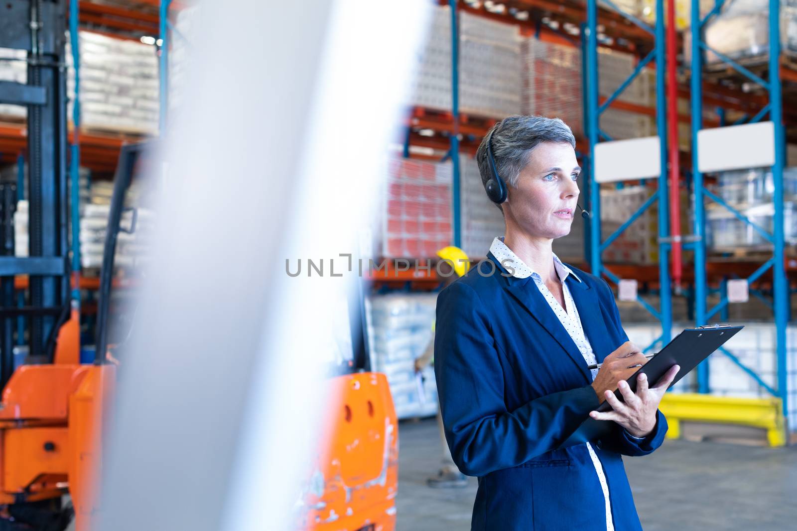 Female manager with headset and clipboard looking away in warehouse by Wavebreakmedia