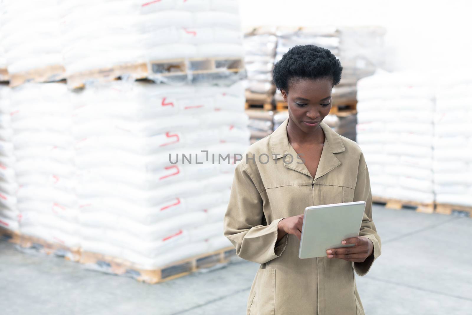 Front view of beautiful young African-american female worker working on digital tablet in warehouse. This is a freight transportation and distribution warehouse. Industrial and industrial workers concept