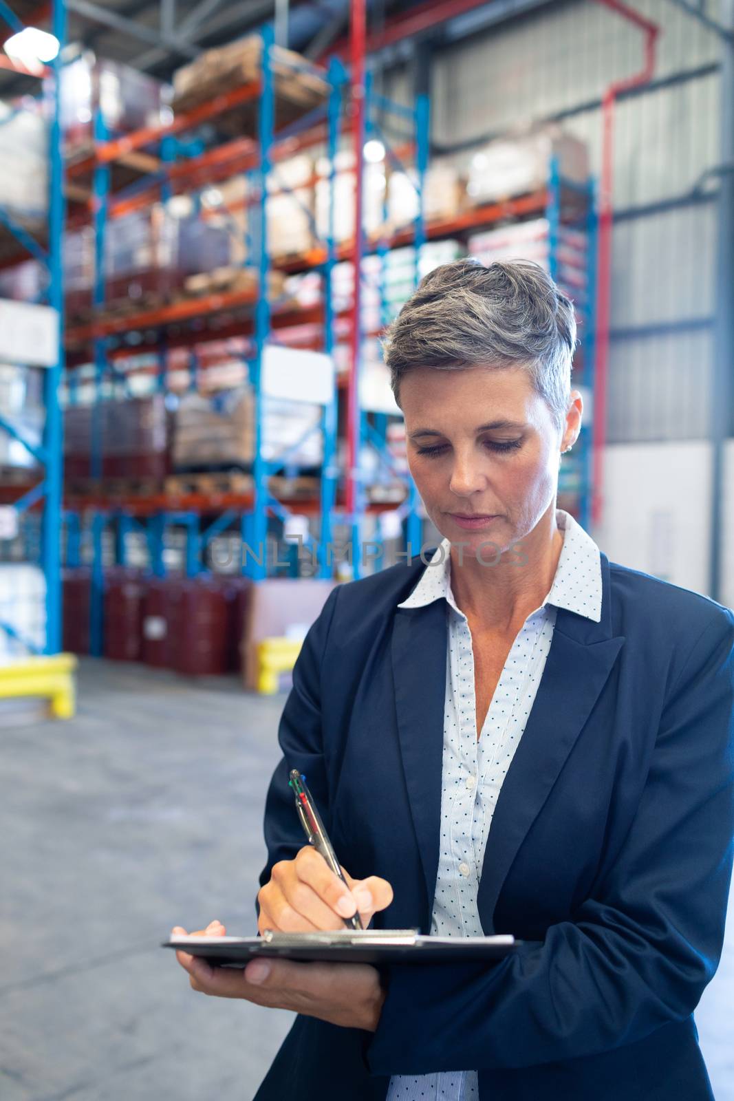 Close-up of beautiful mature Caucasian female manager writing on clipboard in warehouse. This is a freight transportation and distribution warehouse. Industrial and industrial workers concept