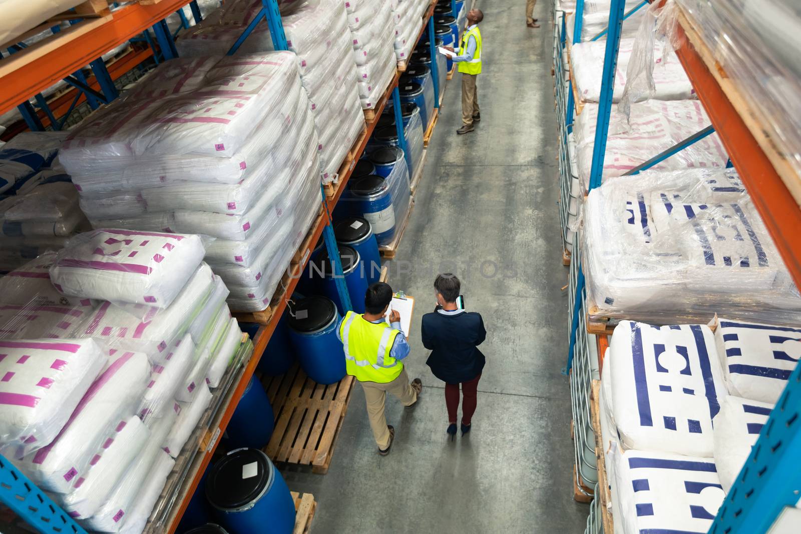 High angle view of Caucasian female manager and Asian male worker in yellow vest discussing over clipboard in warehouse. This is a freight transportation and distribution warehouse. Industrial and industrial workers concept