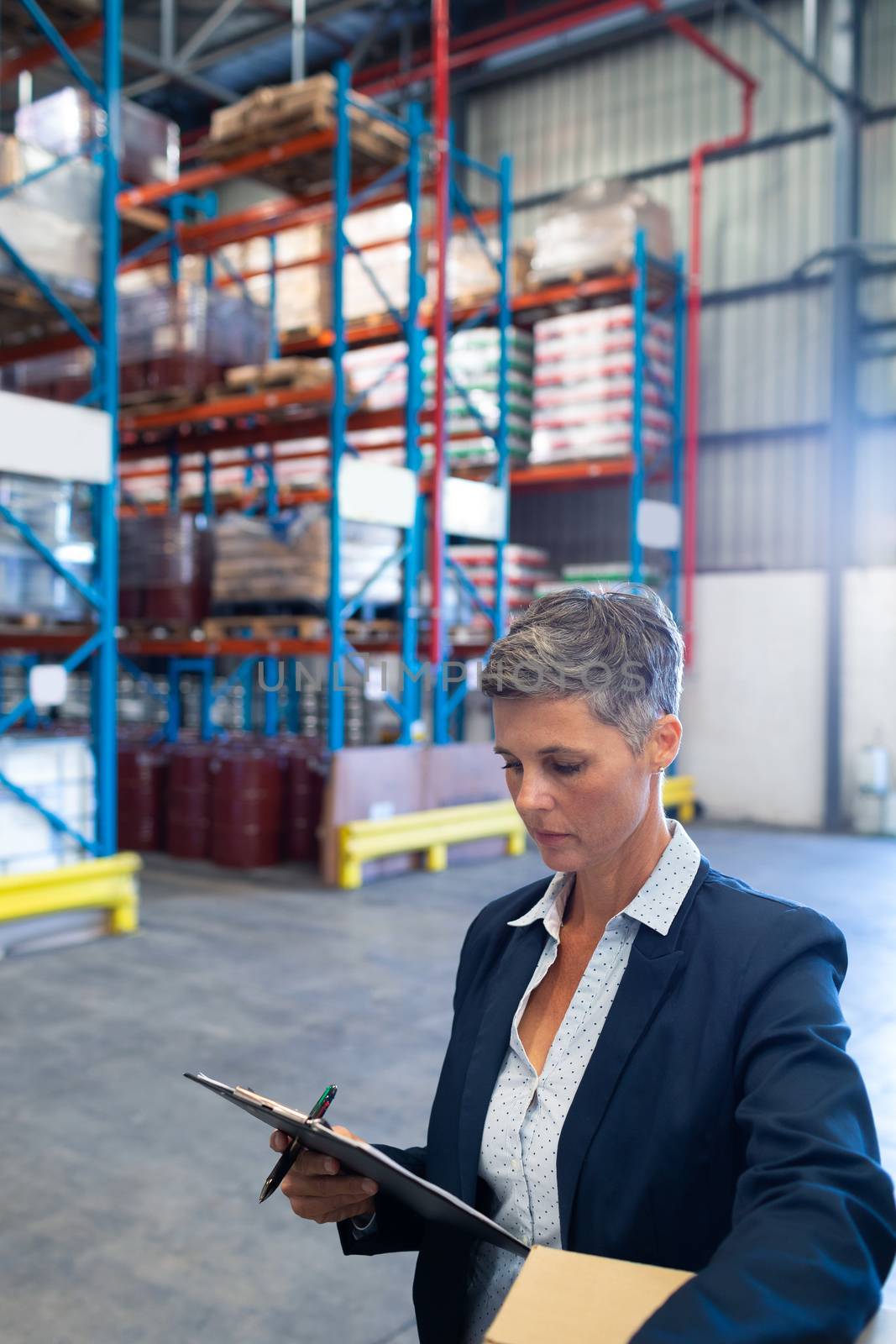 Close-up of beautiful mature Caucasian female manager checking stocks on clipboard in warehouse. This is a freight transportation and distribution warehouse. Industrial and industrial workers concept