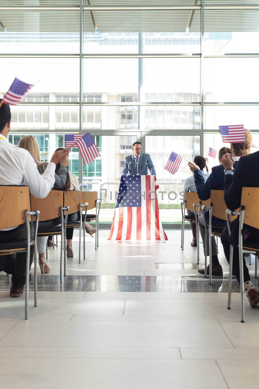 Rear view of group of diverse business people with flags listening mature Caucasian businessman presentation