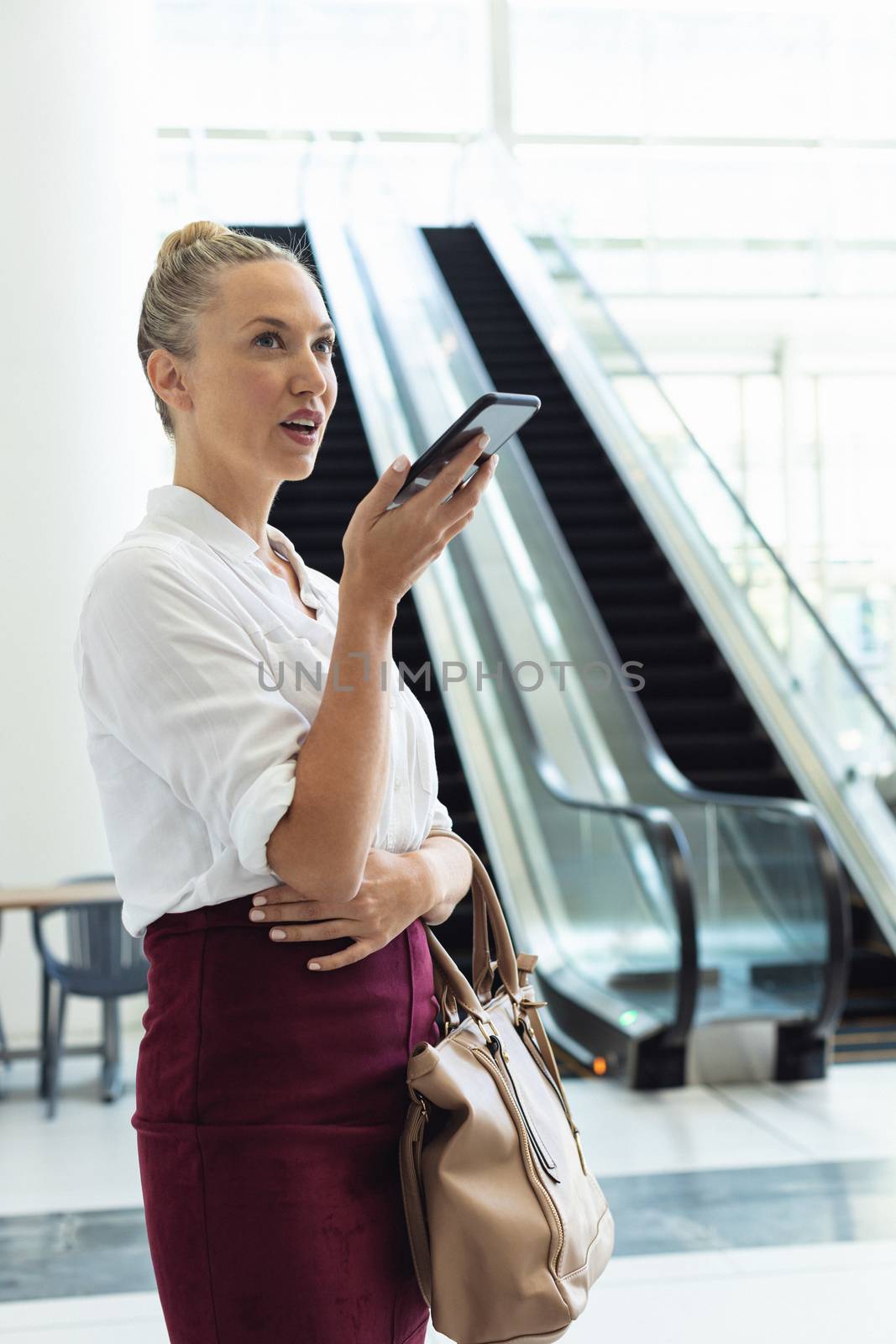 Young Caucasian businesswoman speaking on mobile phone while standing in modern office by Wavebreakmedia