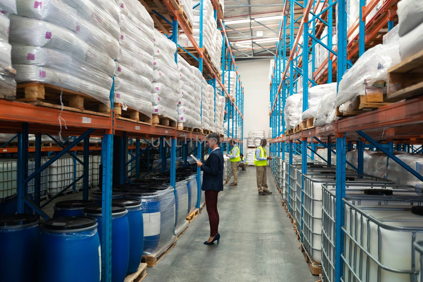 Side view of diverse warehouse staff checking stocks in aisle in warehouse. They are holding clipboards and writing in it. This is a freight transportation and distribution warehouse. Industrial and industrial workers concept
