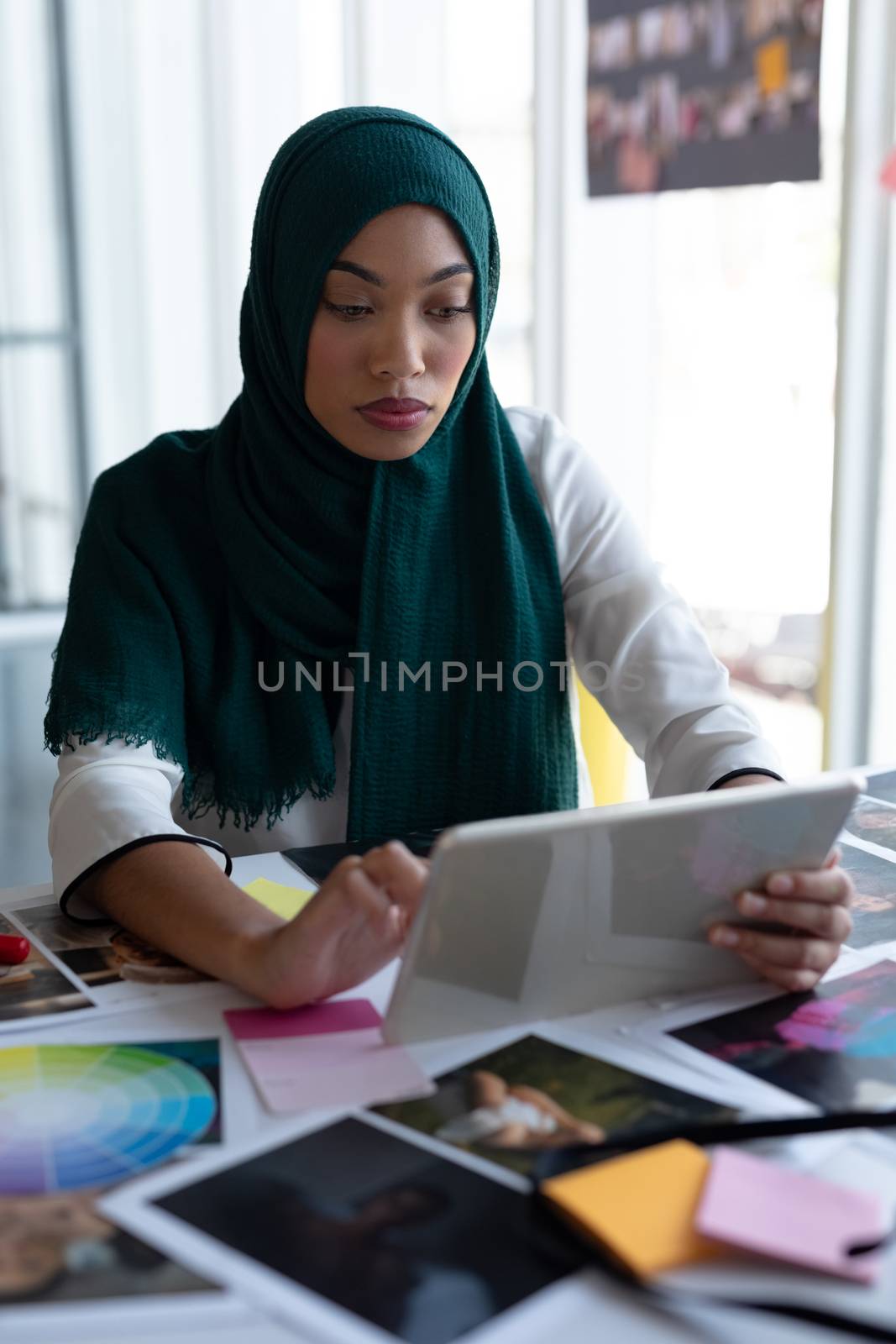 Portrait of mixed race female graphic designer in hijab using digital tablet at desk in office. This is a casual creative start-up business office for a diverse team