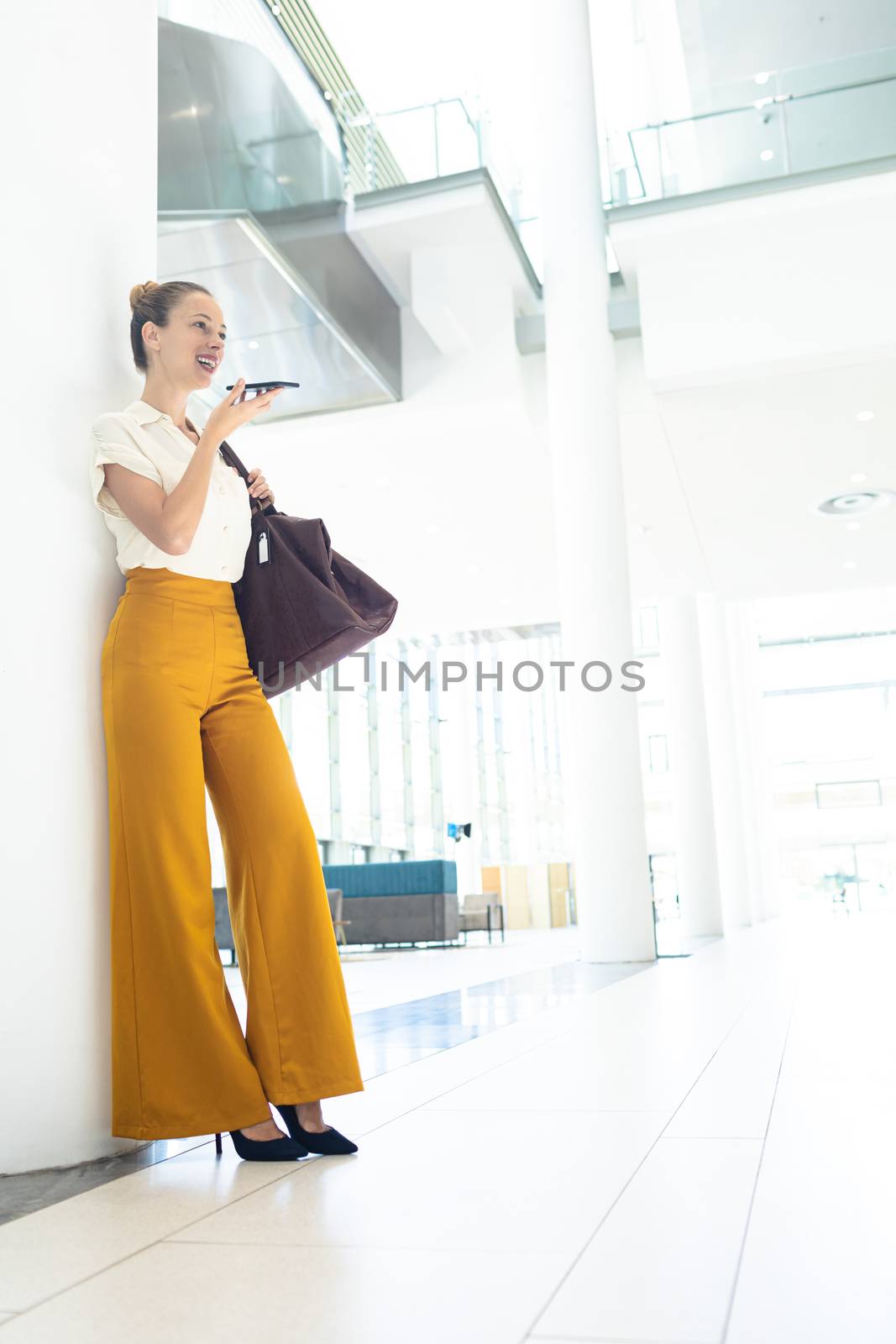 Caucasian female executive speaking on mobile phone while standing in modern office by Wavebreakmedia