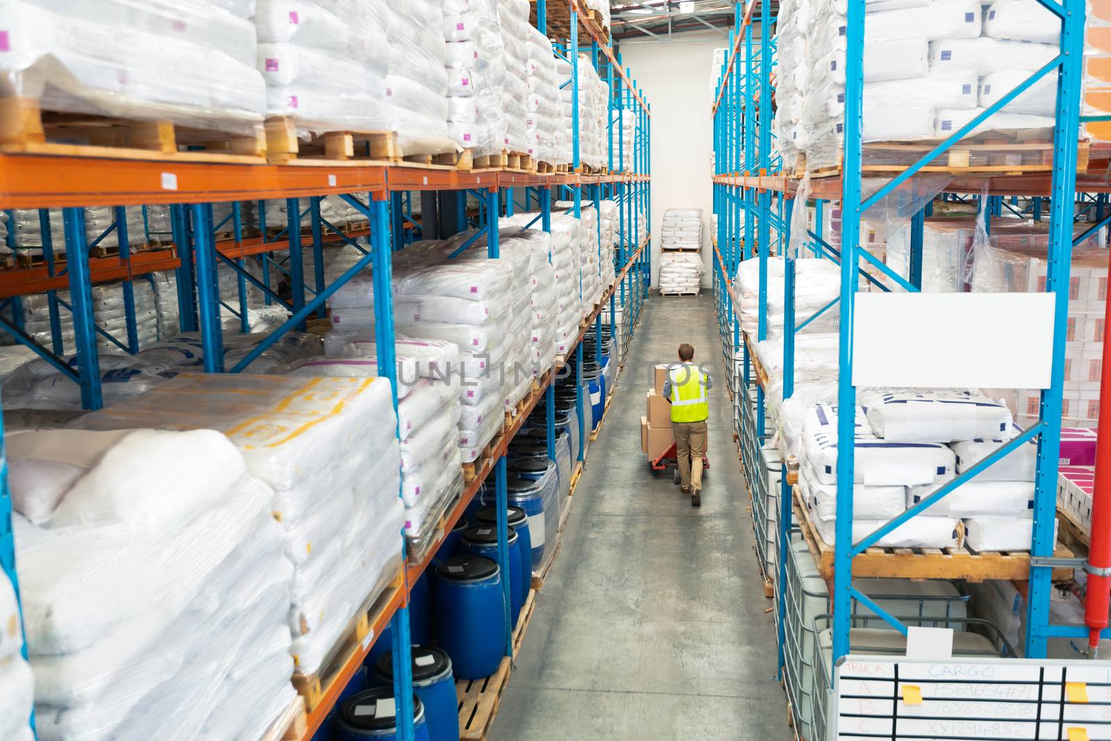 High angle view of hardworking mature African-american worker carrying boxes on pallet jack in warehouse. This is a freight transportation and distribution warehouse. Industrial and industrial workers concept