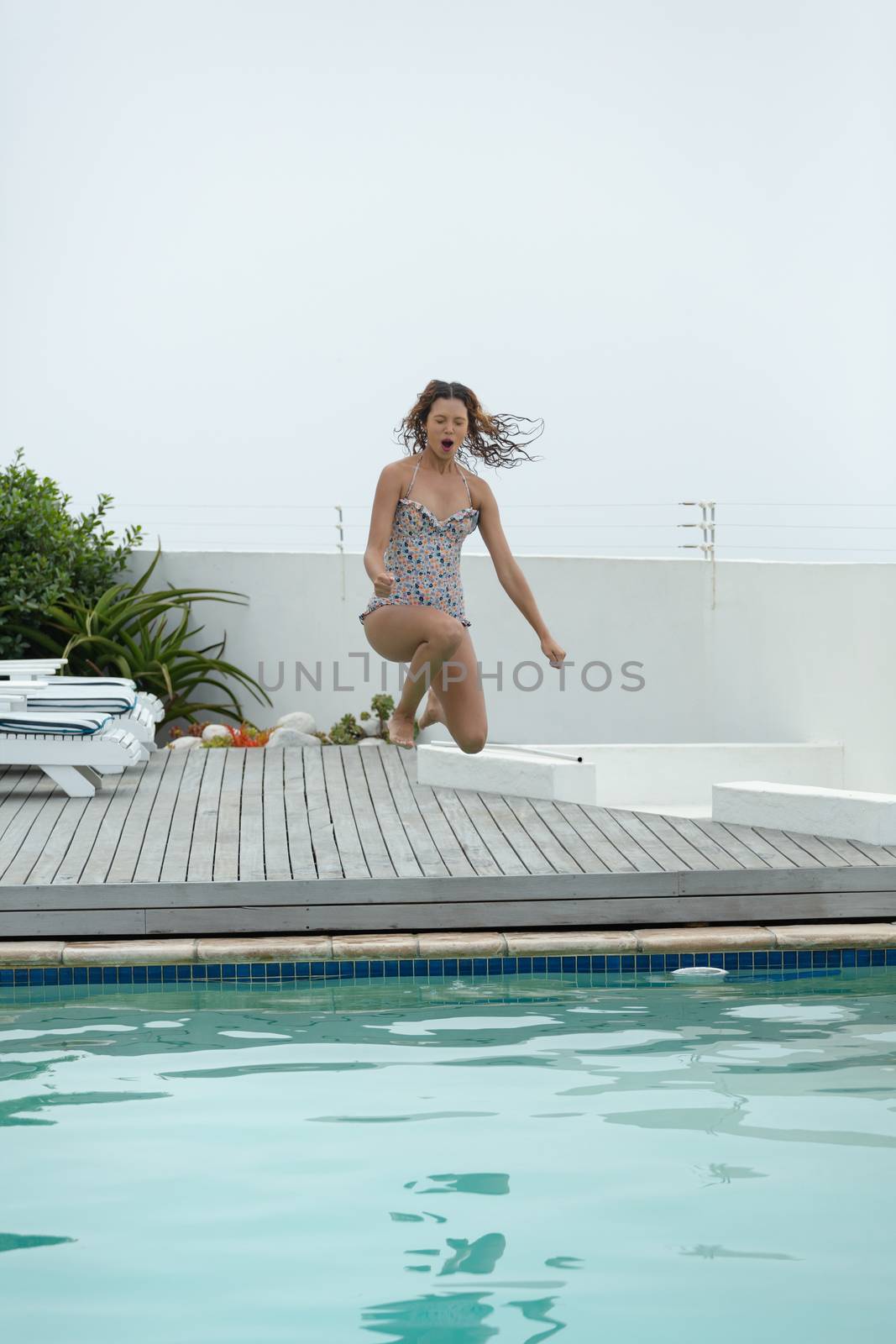 Woman jumping in swimming pool at the backyard of home by Wavebreakmedia