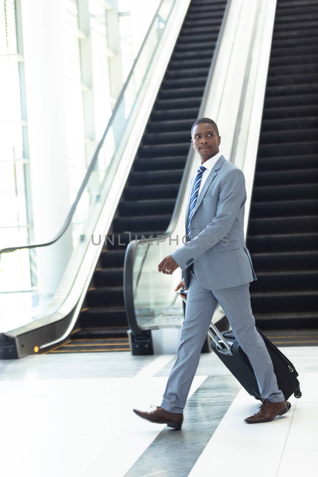 Young African-american executive walking with suitcase in hall by Wavebreakmedia
